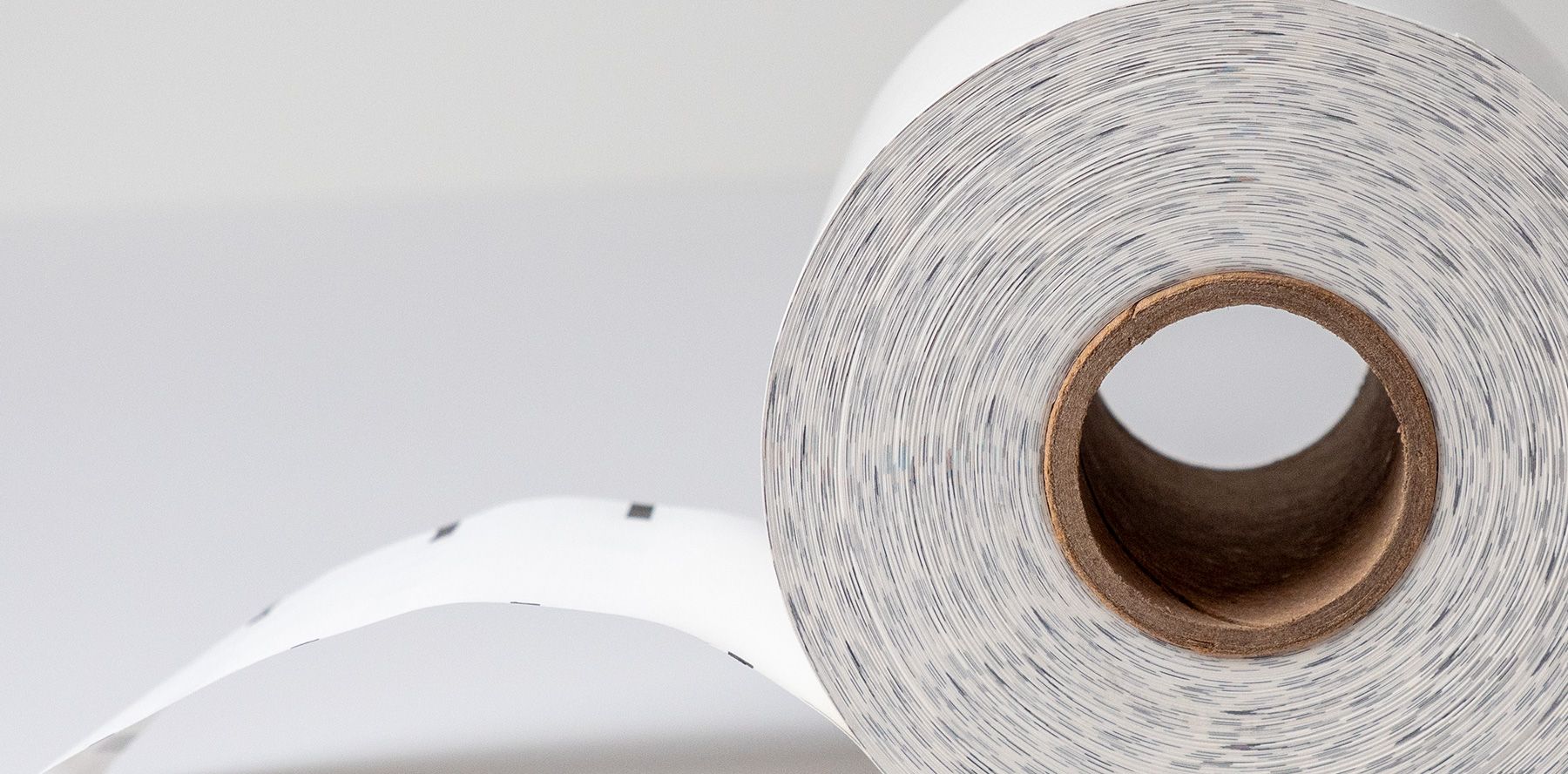 Roll of thermal receipt paper with label edge unspooling, on a gray background.
